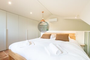 A modern bedroom with a large bed, white linens, and a circular wall decoration. - Villa Analoma - Seignosse - Pool - Beach (Seignosse)