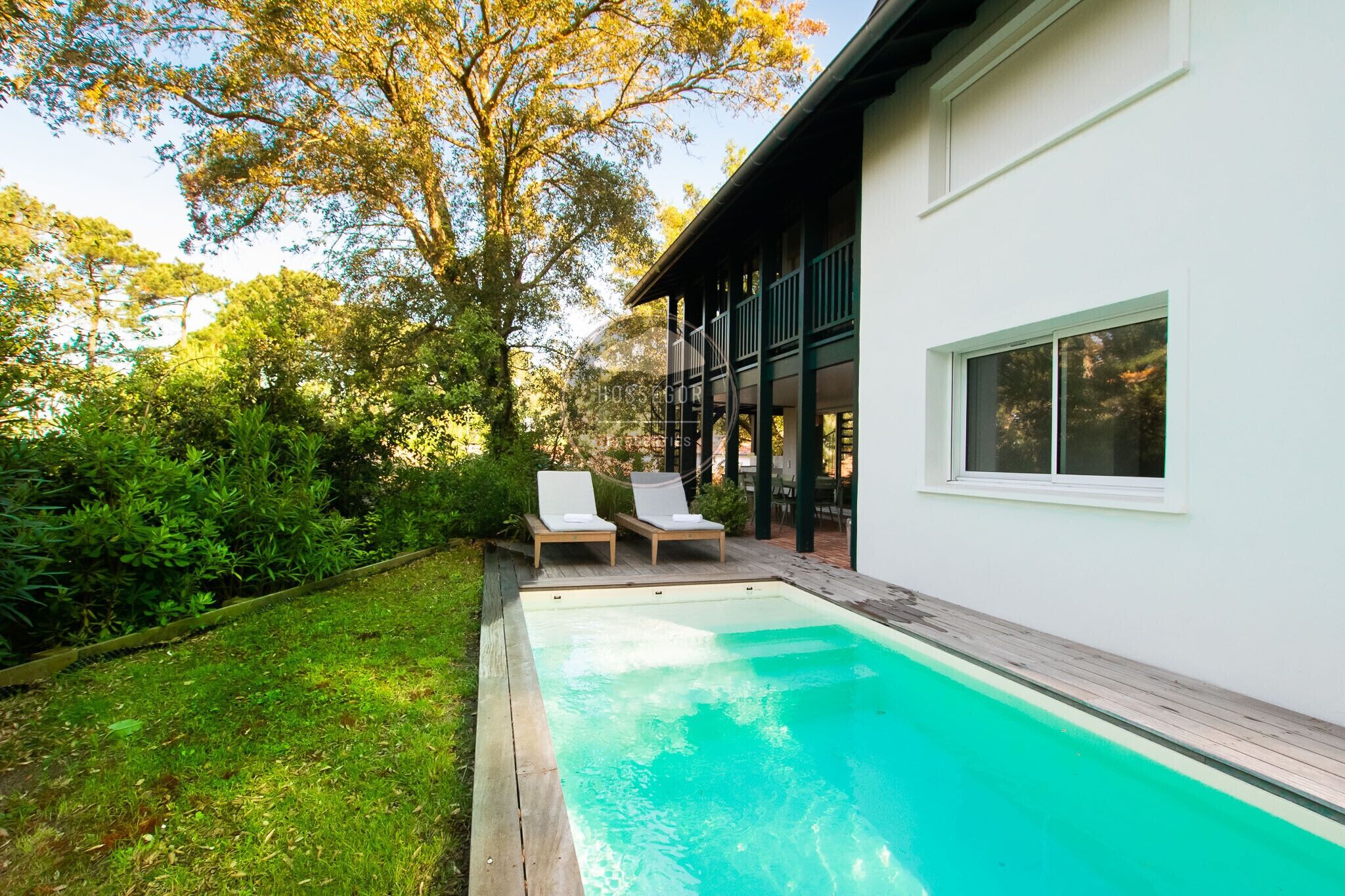 A modern house with a swimming pool, two lounge chairs, and a garden.