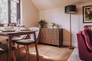A dining area with a wooden table set for two, a cabinet with a plant, and a red sofa. - The Damson Loft, Cosy, Central Bowness, Parking (Bowness-on-Windermere)