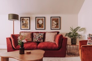 A red sofa with floral cushions, a wooden coffee table, and a floor lamp. - The Damson Loft, Cosy, Central Bowness, Parking (Bowness-on-Windermere)