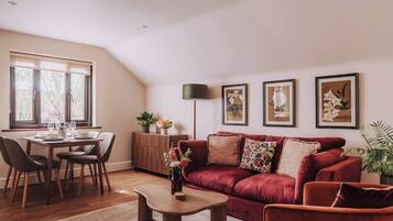 A living room with a red sofa, a coffee table, a dining area with a table and chairs, and a large window with blinds.