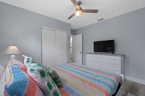 Ein Schlafzimmer mit Bett, Deckenventilator, Fernseher und Kommode.