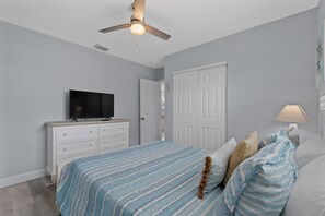Een slaapkamer met een bed, een televisie op een dressoir, een plafondventilator en een deur.