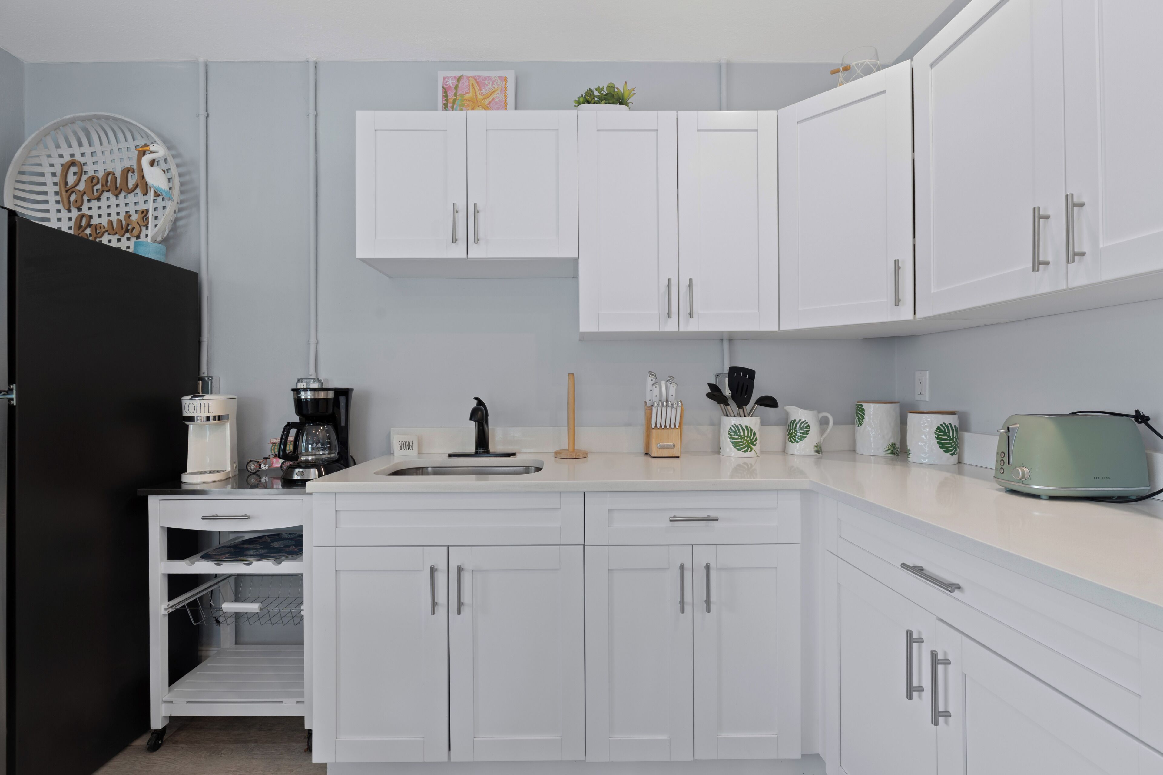 Une cuisine moderne avec des meubles blancs, une machine à café, un grille-pain et un évier.