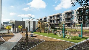 Ein Spielplatz mit vielfältigen Spielgeräten, umgeben von einer angelegten Grünfläche mit Gras und Pflanzen.