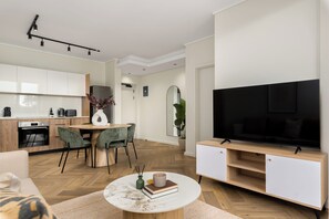 Un salon moderne doté d’un téléviseur à écran plat, d’un coin repas avec une table ronde et d’une cuisine avec des meubles en bois.