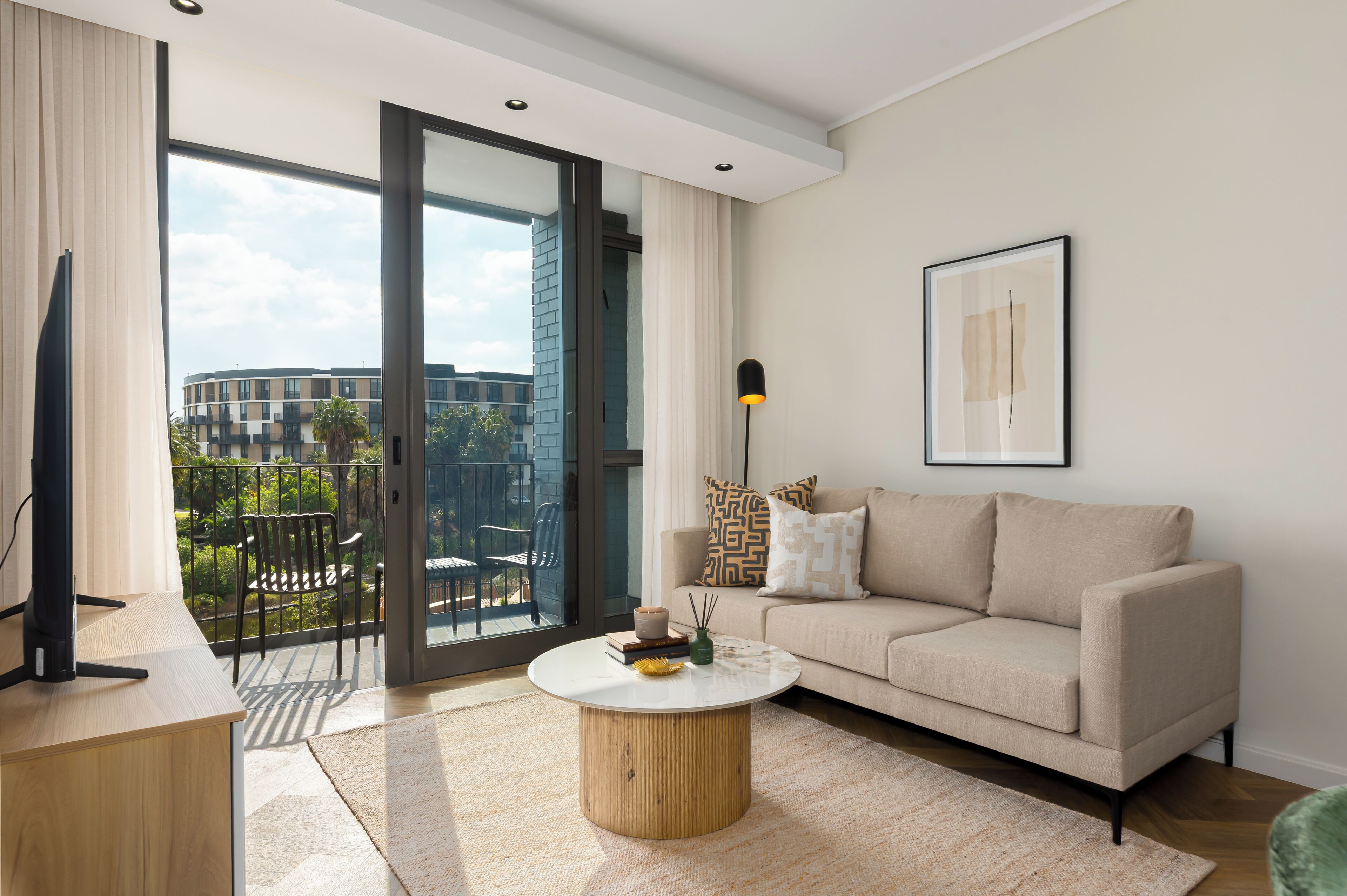 A modern living room with a sofa, coffee table, and a view of a building through a glass door.