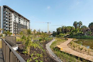 Ein modernes Gebäude mit mehreren Balkonen, eine angelegte Grünfläche mit einem gewundenen Holzweg und ein Gewässer.