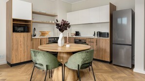Eine moderne Küche mit einem runden Holztisch, zwei grünen Stühlen, einem Edelstahlkühlschrank und Holzschränken.