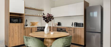 Cocina moderna con una mesa redonda de madera, dos sillas verdes, un refrigerador de acero inoxidable y armarios de madera.