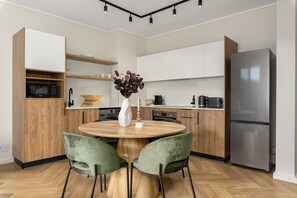 Eine moderne Küche mit einem runden Holztisch, zwei grünen Stühlen, einem Edelstahlkühlschrank und Holzschränken.