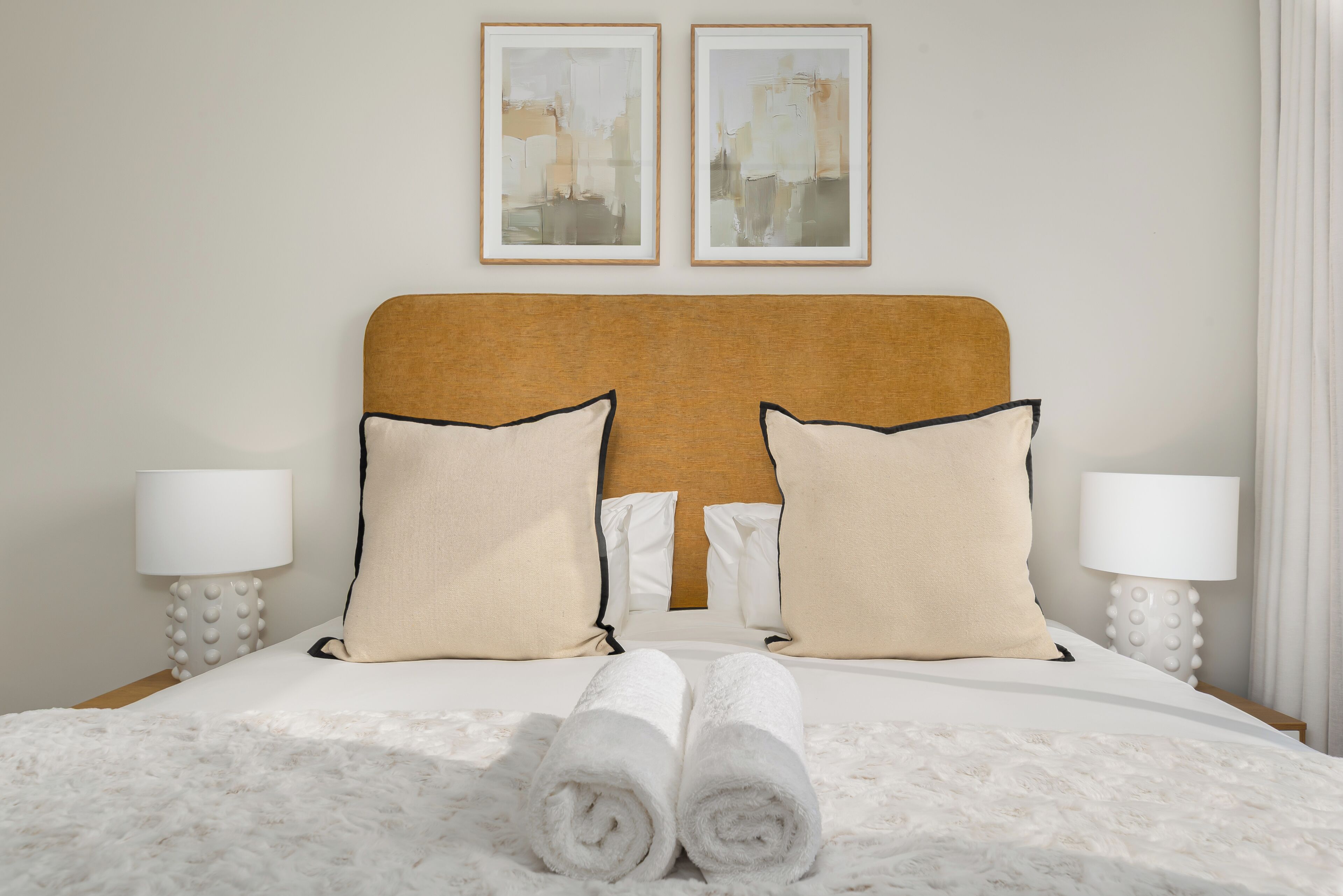 Una cama bien tendida con cabecera, dos almohadas y toallas enrolladas.