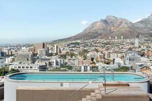 Una piscina en la azotea con un cartel de 'No Diving', rodeada por un paisaje urbano que incluye edificios y montañas al fondo.