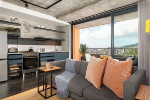 A modern kitchen with a built-in oven and microwave, a dining area with a gray sofa and orange cushions, and a large window offering a city view. - FortyOnL | Table Mountain Retreat (Cape Town)