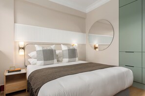 A bedroom with a bed, bedside lamps, a nightstand, a mirror, and a wardrobe. - Charlie and the Chairman | Elegant Urban Stay (Cape Town)