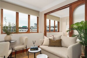 Ein modernes Wohnzimmer mit einer Couch, Sesseln, einem kleinen Tisch und einem großen Fenster mit Blick auf die Stadt.