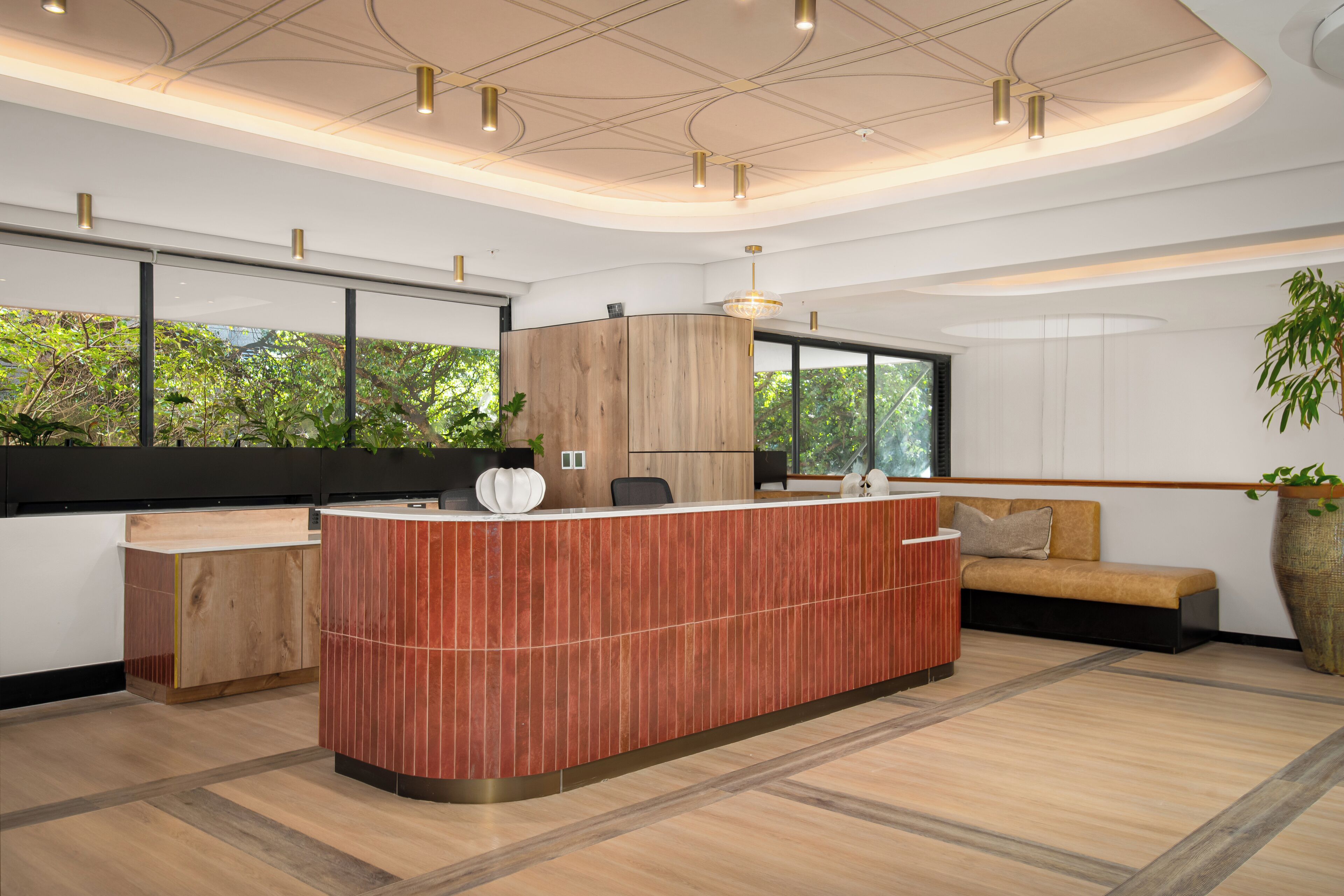 A modern reception area with a wooden reception desk, a sofa, and a large window with a view of greenery.