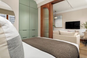 Ein modernes Schlafzimmer mit einem Bett, einem grünen Kleiderschrank, einer Holztür, einem Fernseher, einem Sofa und einer Pflanze.