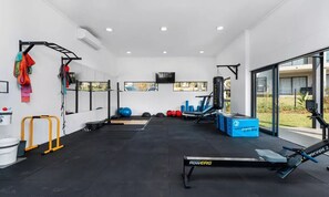 A gym with exercise equipment, a rowing machine, and a TV screen.