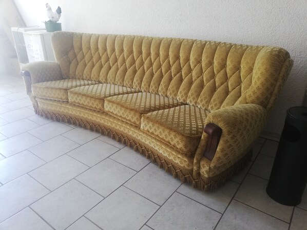 A sofa with a tufted backrest and patterned upholstery, positioned against a wall with a tiled floor.