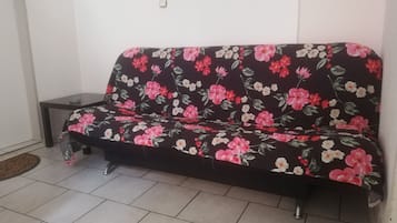 A dark-colored sofa with a floral pattern, positioned against a white wall in a room with tiled flooring.