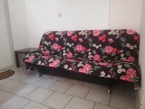 Un sofá de color oscuro con estampado floral, ubicado frente a una pared blanca en una habitación con suelo de baldosas.