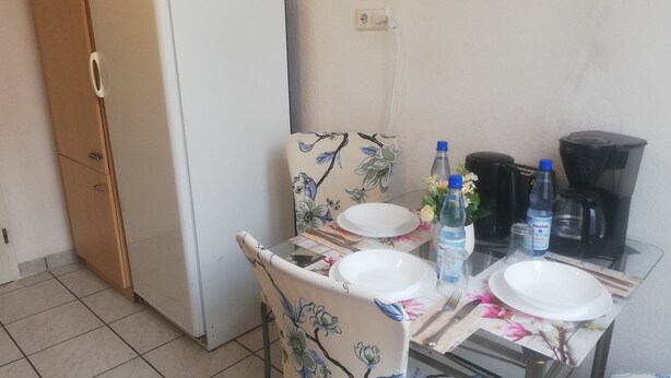 Et spiseområde med et bord dækket til to personer, et køleskab og en kaffemaskine.