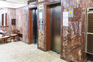 Um espaço de elevador com paredes de mármore, uma cadeira de madeira e um aviso com um rosto sorridente.