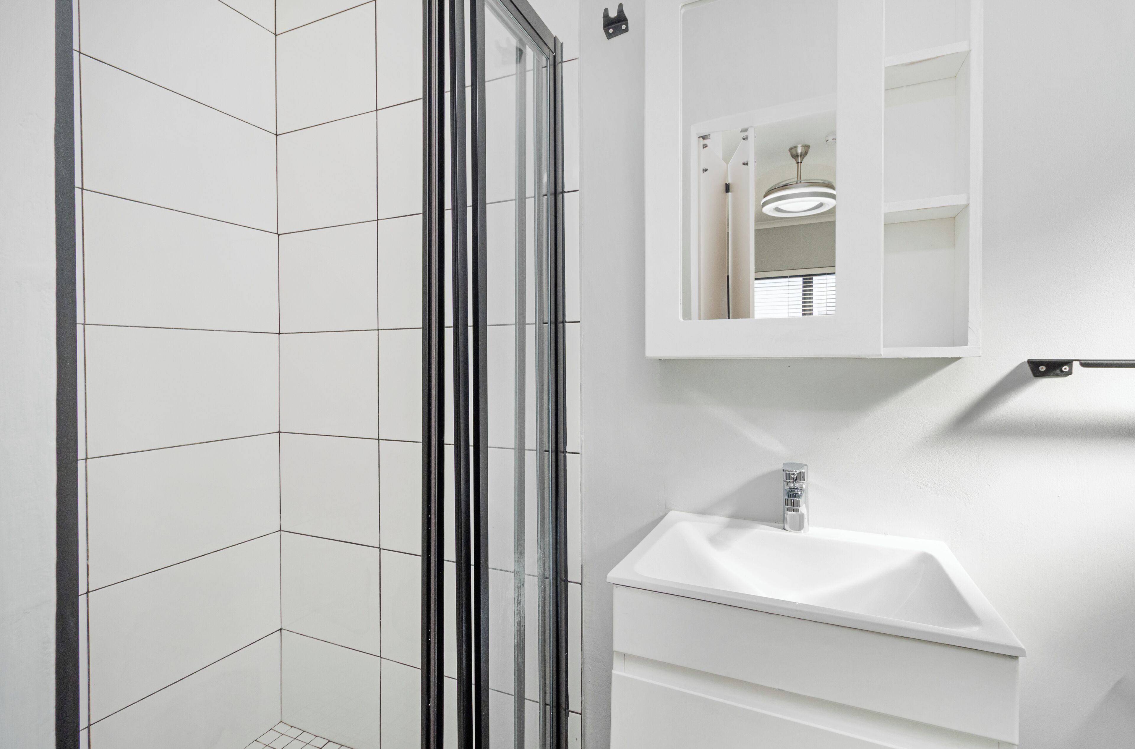 Ein modernes Badezimmer mit Duschkabine aus Glas, einem weißen Waschbecken und einem Spiegel darüber.