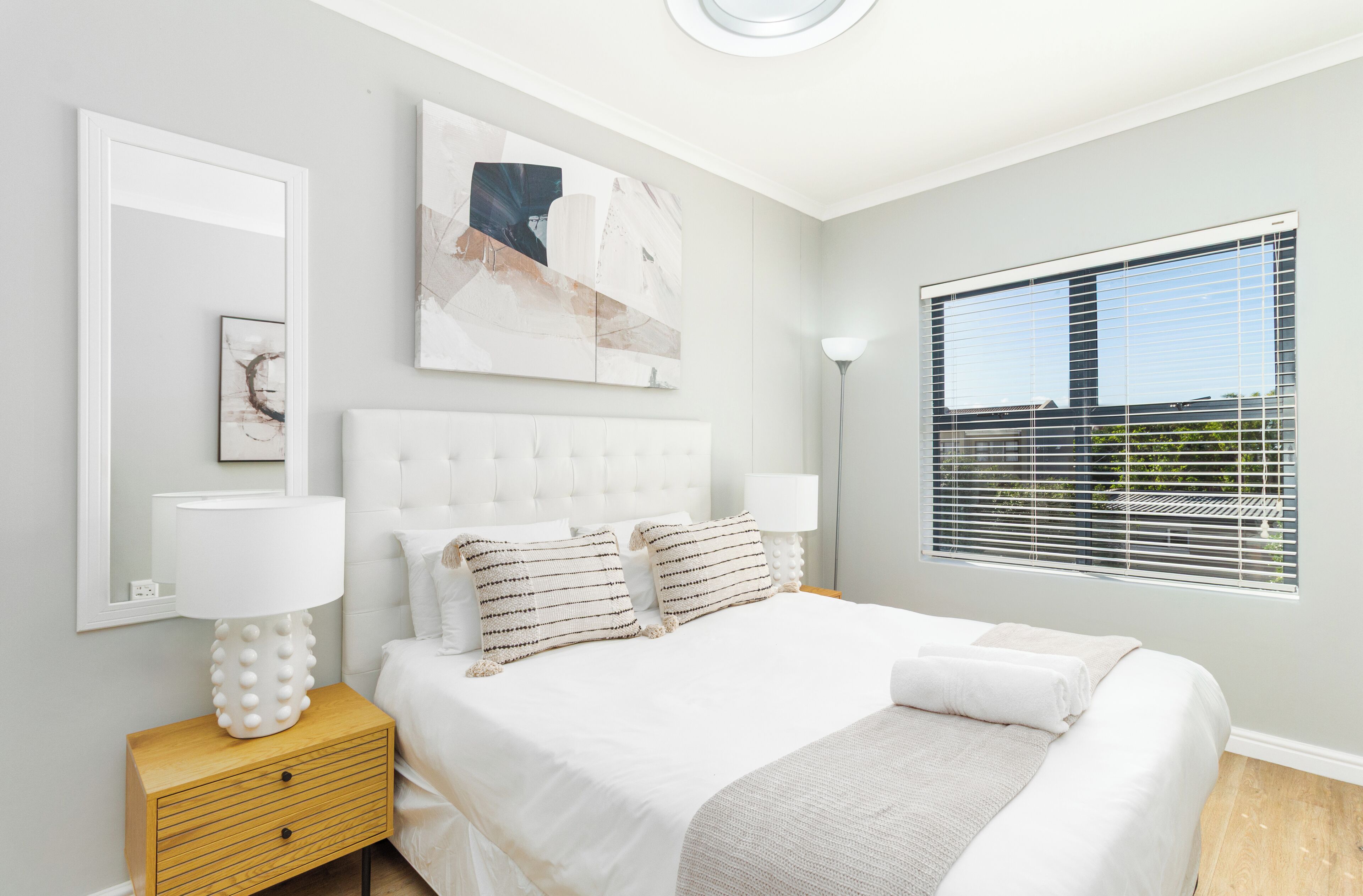 Un dormitorio moderno con una cama grande, lámparas de noche, una mesita de noche y una ventana con persianas.
