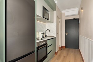 A narrow hallway leading to a dark door, with a kitchen area on the left featuring a refrigerator, oven, and coffee maker. - Charlie and the Chairman | Elegant CBD Retreat (Cape Town)