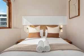 A hotel room with a large bed, a headboard with integrated lighting, a window with a view of the city, and a neatly made bed with towels. - Charlie and the Chairman | Elegant CBD Retreat (Cape Town)