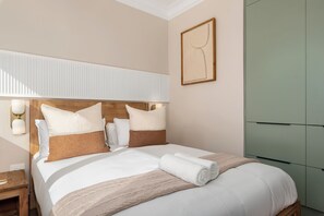 Un lit bien fait, avec une literie blanche et des touches de couleur marron, une lampe de chevet et une table de chevet en bois.