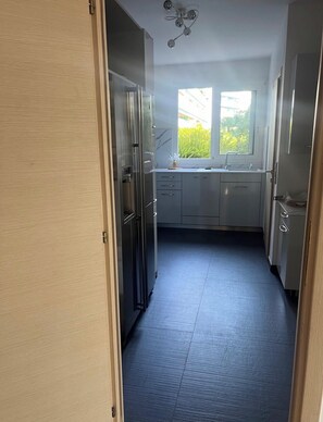 Eine schmale Küche mit Fenster, Kühlschrank und Schränken.