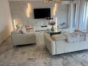 Ein modernes Wohnzimmer mit zwei Sofas, einem Couchtisch, einem Wand-Fernseher und einem Marmorboden.
