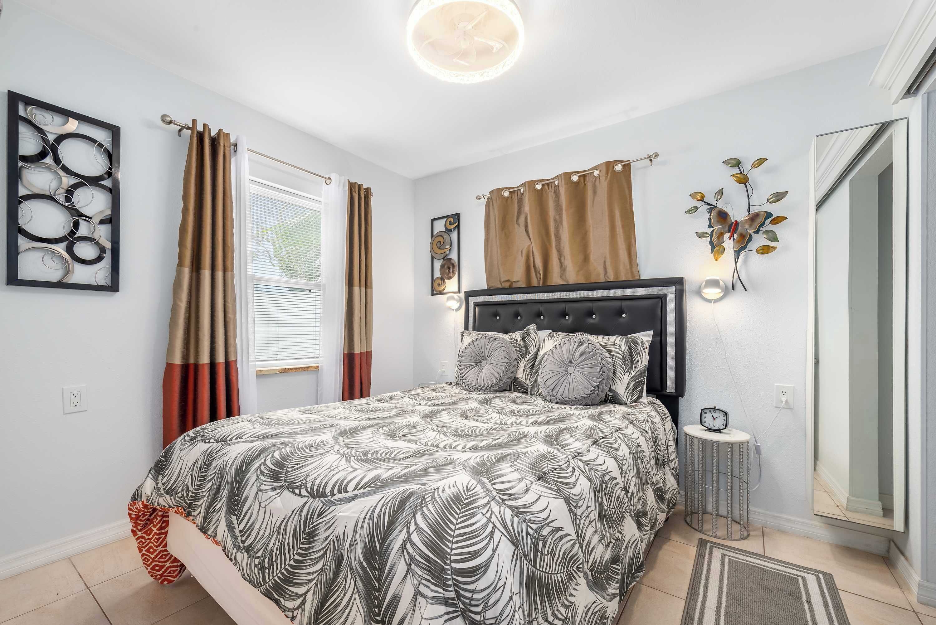 Een slaapkamer met een bed, gordijnen, een wandklok en een spiegel.