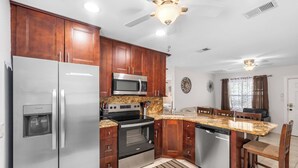 A kitchen with wooden cabinets, stainless steel appliances, a granite countertop, and a ceiling fan. - 3 Min Walk to Beach | Private Triplex Retreat (Indian Rocks Beach)