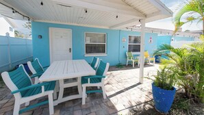 A covered outdoor seating area with a white table and chairs, a door, and a window. - 3 Min Walk to Beach | Private Triplex Retreat (Indian Rocks Beach)