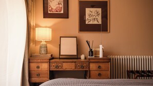 Ein Hotelzimmer mit einem Bett, einem Schreibtisch mit Lampe, einem gerahmten Bild, einem Heizkörper und einem Fenster mit Vorhängen.