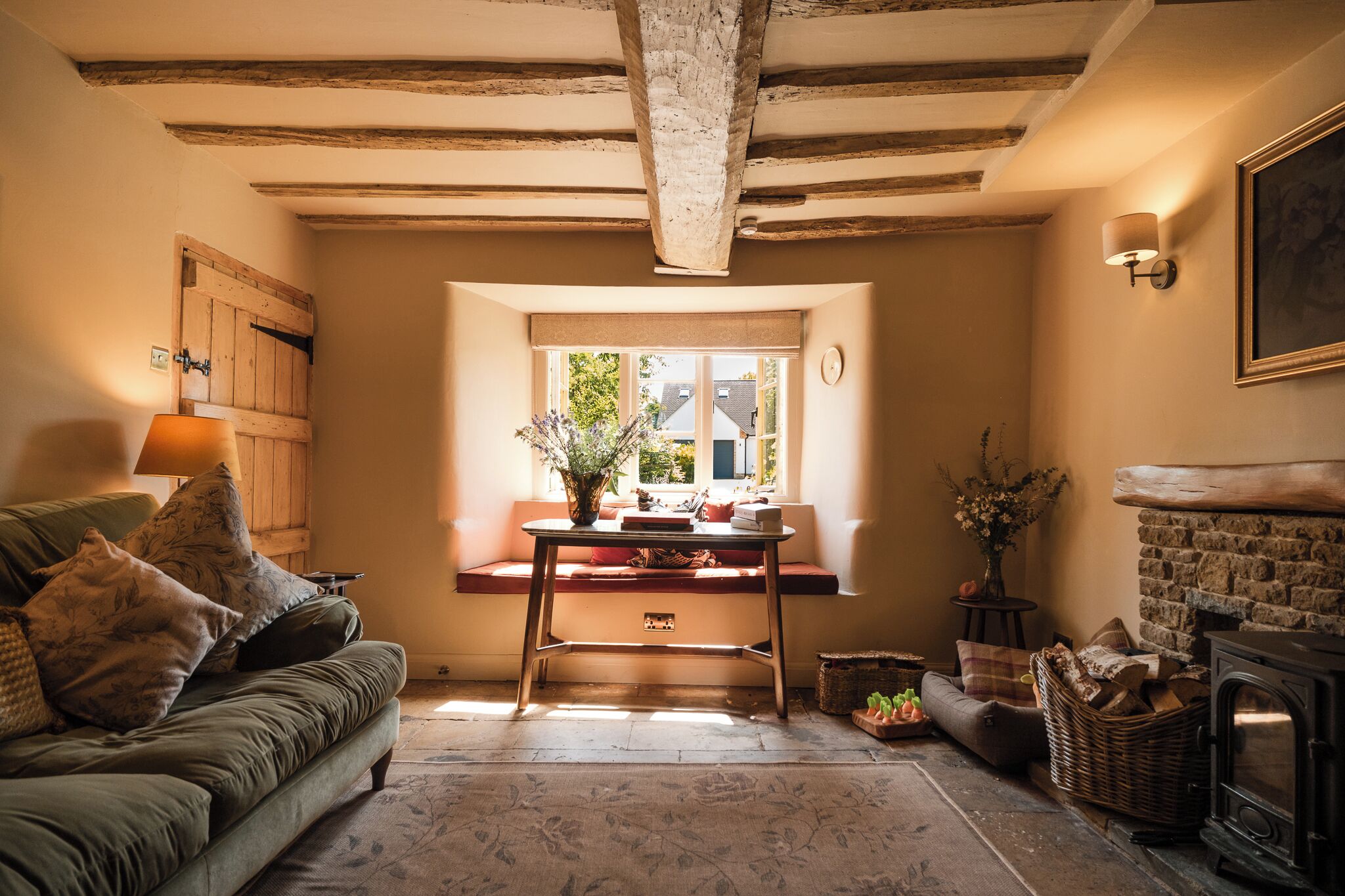 A cozy living room with a sofa, a table with a vase, a fireplace, and a window with a view.