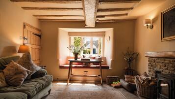 A cozy living room with a sofa, a table with a vase, a fireplace, and a window with a view.