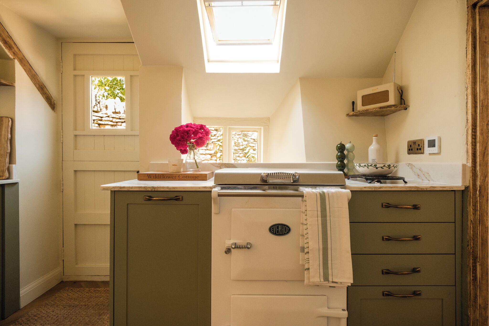 A compact kitchen with a built-in oven, a microwave, and a sink. There is a skylight above the sink, and a window with a view of greenery outside.