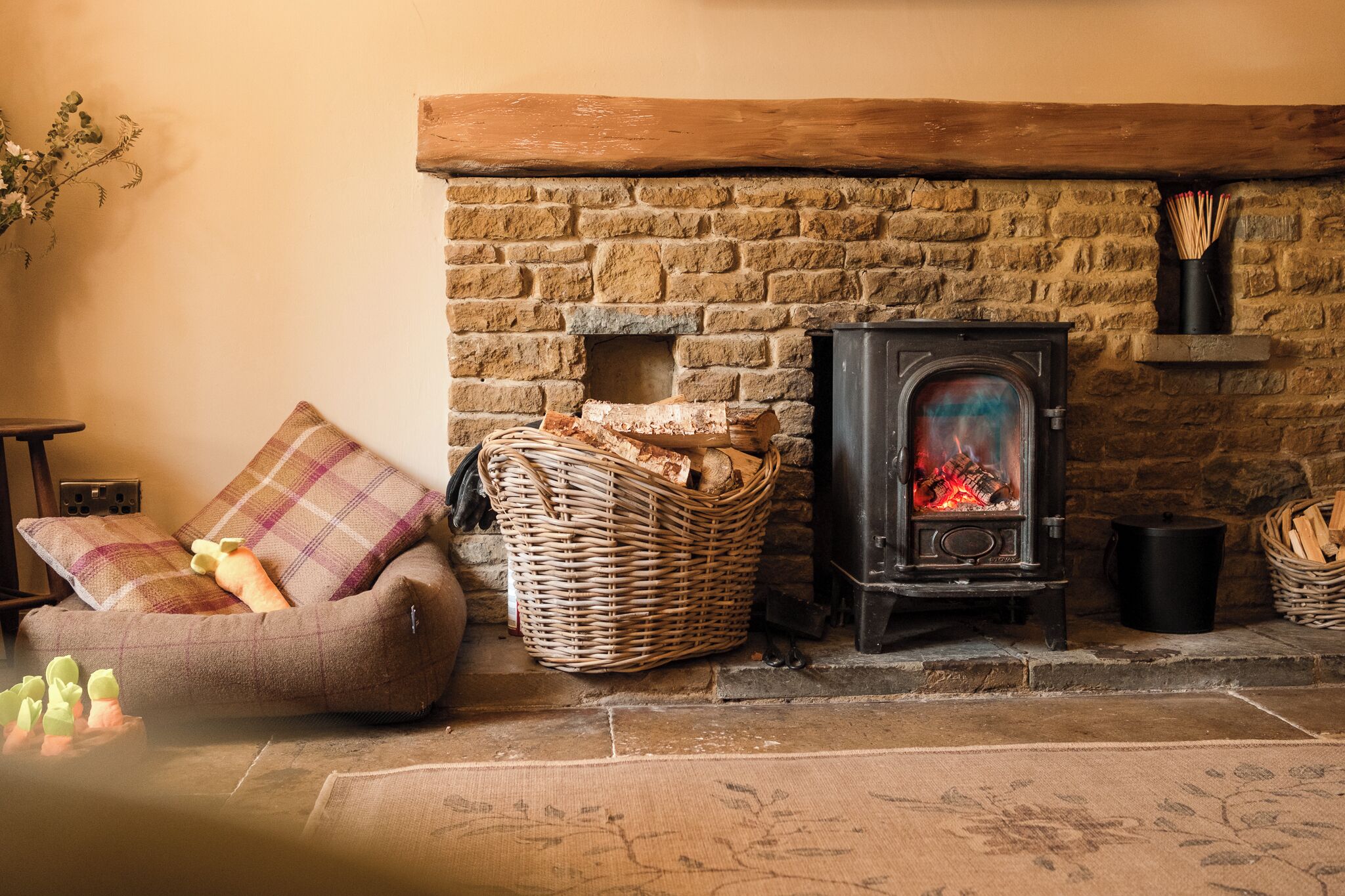 Una habitación acogedora con chimenea de piedra, una cesta de mimbre y un rincón de estar con cojines.