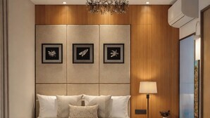 Un dormitorio moderno con una cama grande, una araña, obras de arte enmarcadas en la pared y una mesita de noche con una lámpara.