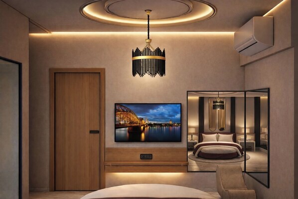 A modern hotel room with a large TV, a chandelier, a bed, and a bedside table.