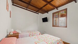 Un dormitorio con dos camas, techo de madera, televisor montado en la pared y ventana con vista al exterior.