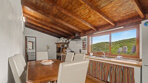A rustic kitchen with a stone oven, wooden ceiling beams, and a view of a green hillside.