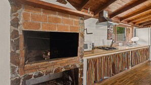 A kitchen with a brick oven, wooden beams, a tiled backsplash, and a striped curtain.