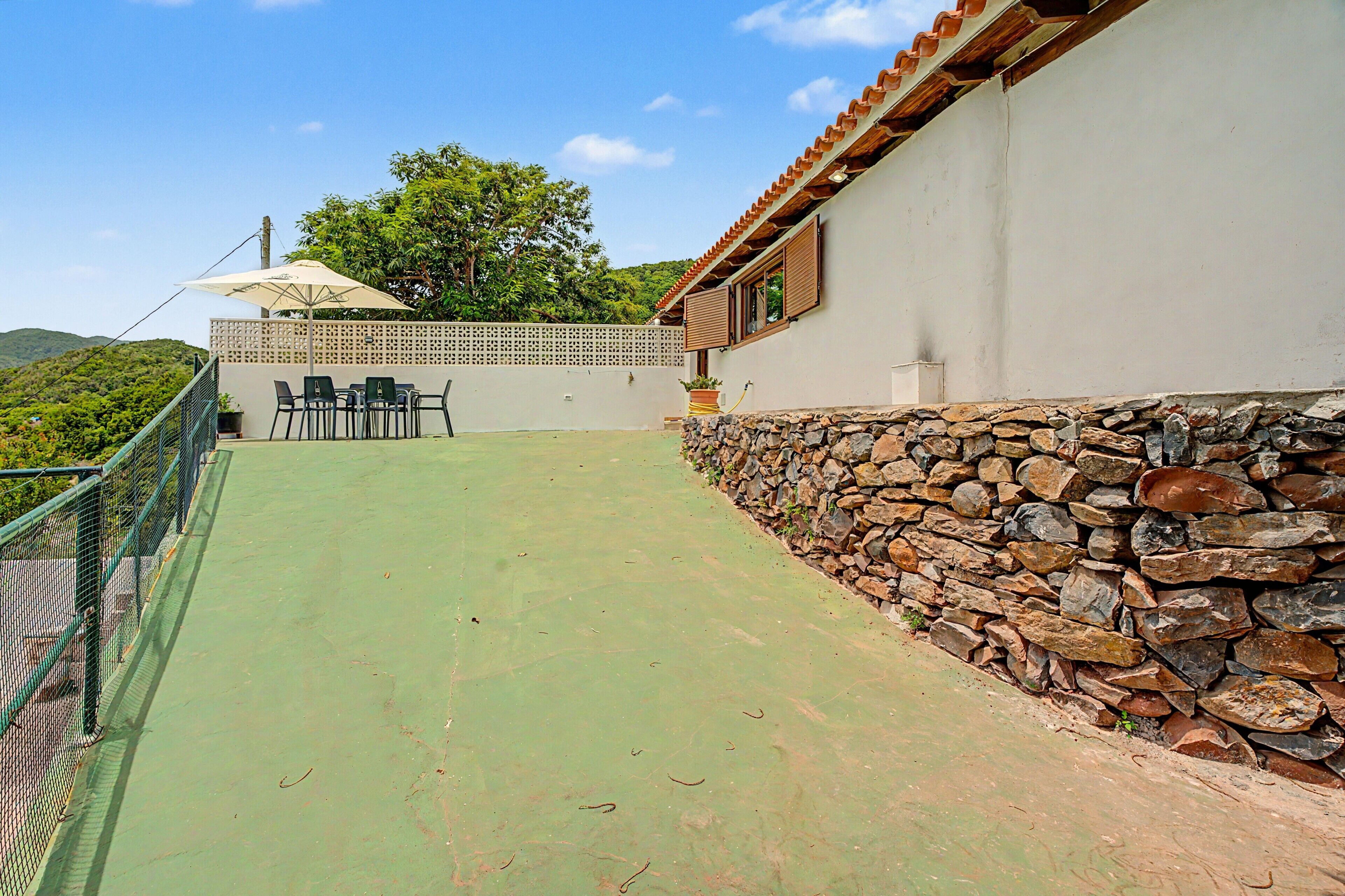 Un patio con mesa y sillas, un muro de piedra y vistas del paisaje circundante.