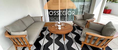 A patio area with a sofa set, two chairs, a round table, and a patterned rug.